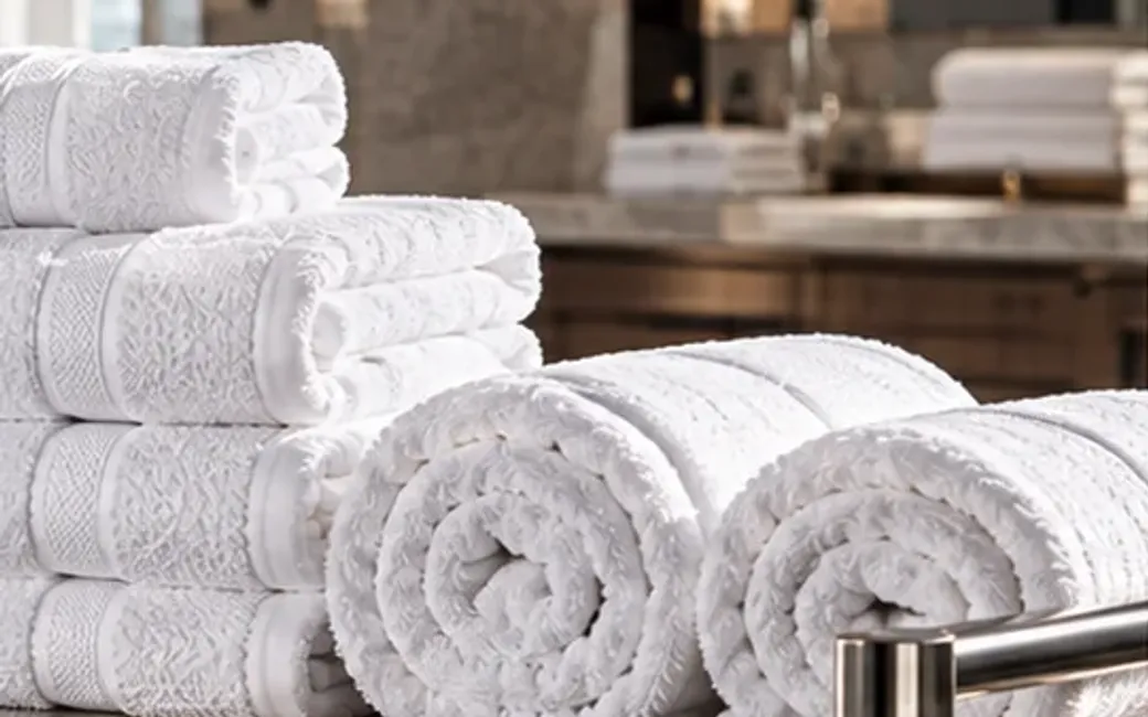 Rolled and folded white terry towels on a metal linen trolley in a hotel-style setting.